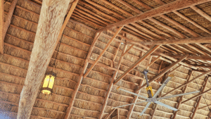 Detailed view of the Island Tiki Hut thatch roof construction with massive wooden beams, hanging lantern, and large industrial ceiling fan.