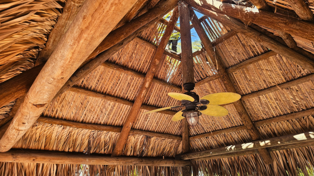 Interior view of an Island Tiki Hut thatched roof with exposed wooden beams and a yellow ceiling fan.